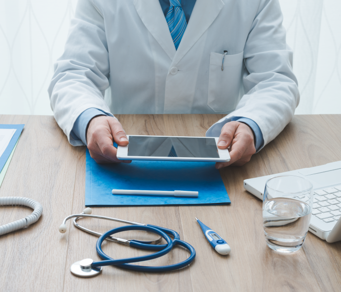 Photo of doctor sitting at desk holding a tablet with a white laptop
